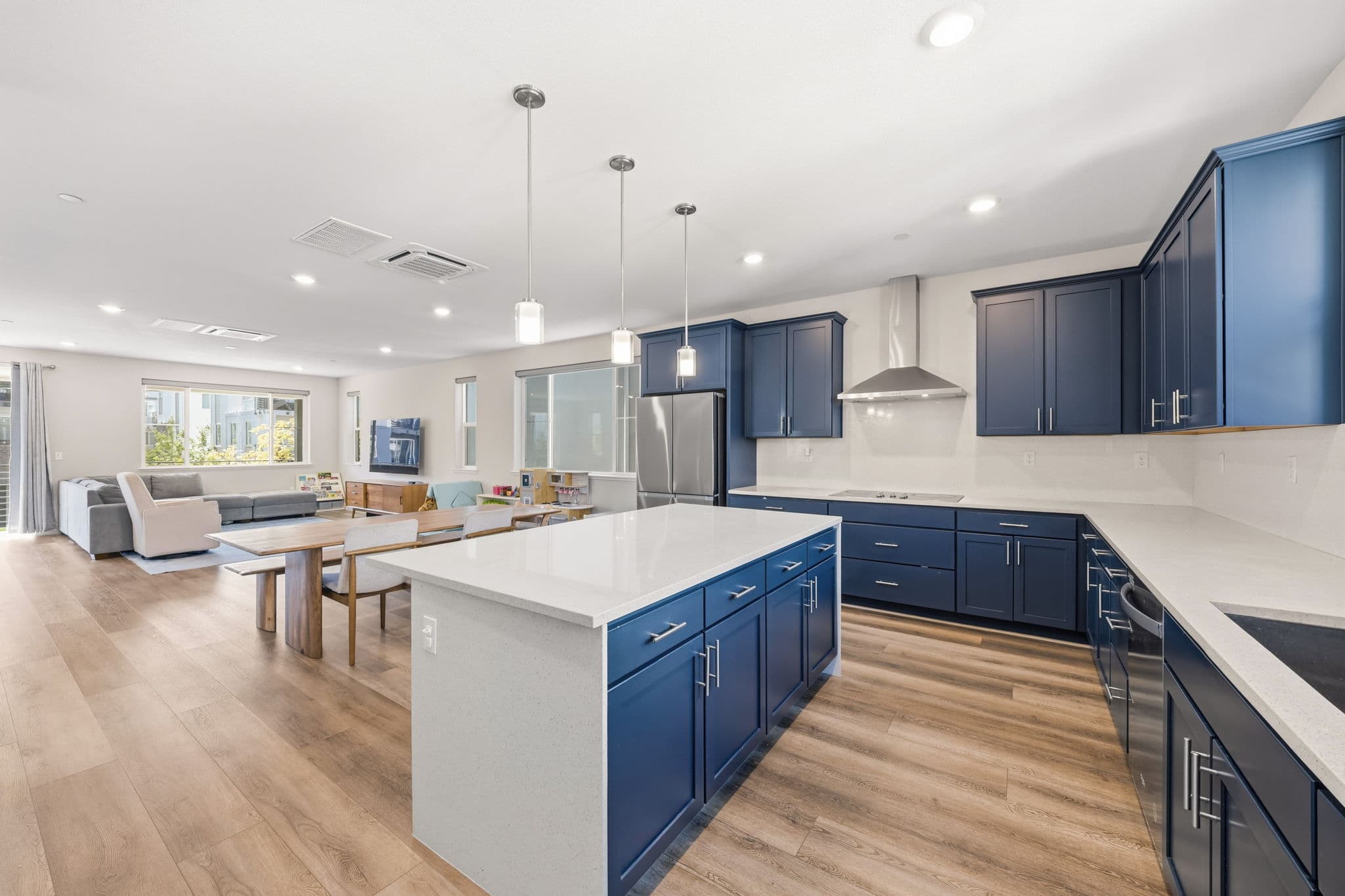 Open-plan second floor — waterfall island and navy kitchen flowing to the sunlit gathering room and balcony