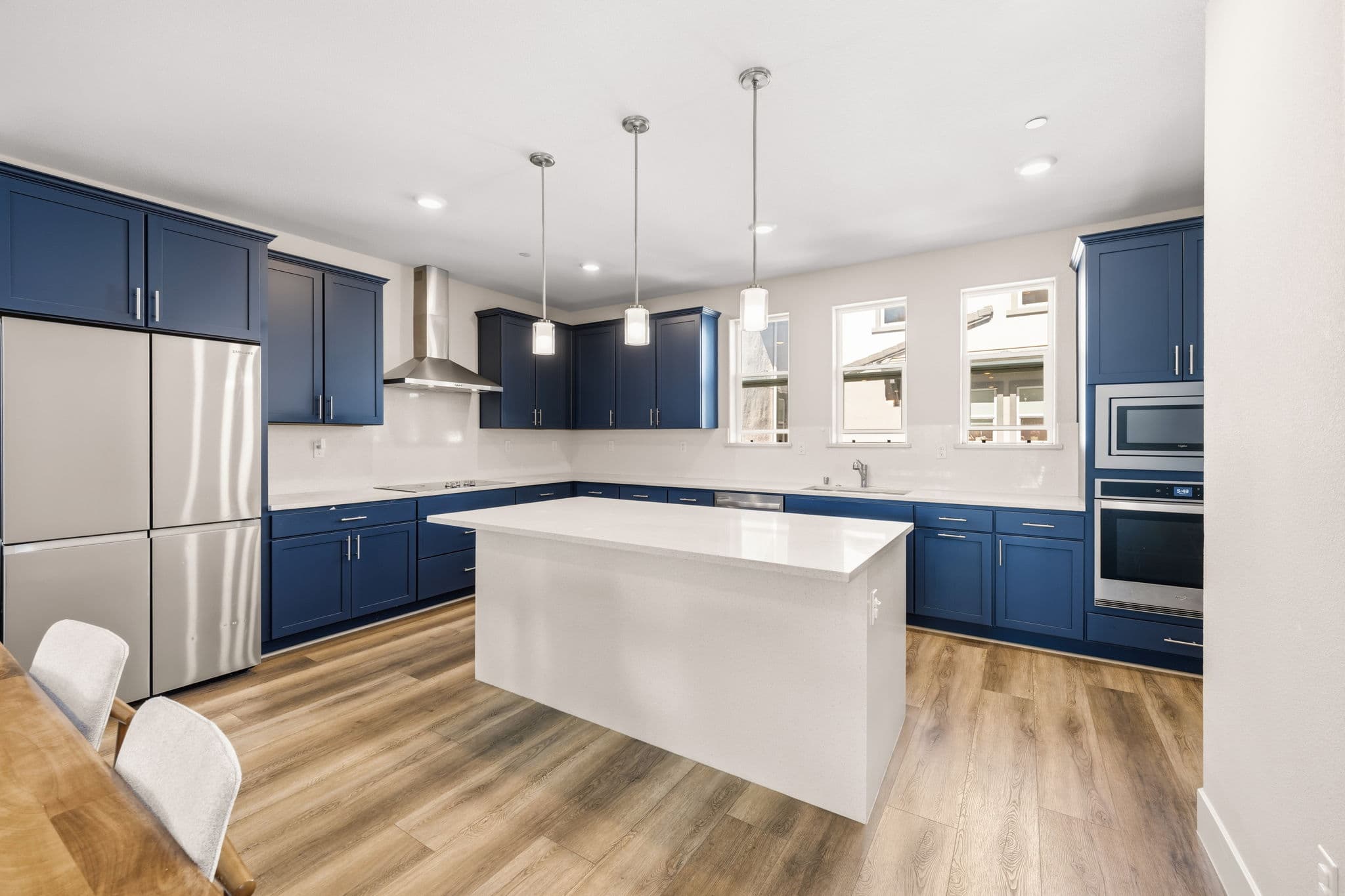 Chef's kitchen — navy shaker cabinets, granite slab backsplash, waterfall island under glass pendants